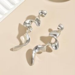 Ένα ζευγάρι μακριά statement σκουλαρίκια σε ασημί-μεταλλική απόχρωση με ρευστό, κυματιστό και αφηρημένο σχήμα, ιδανικά για μια μοντέρνα και εντυπωσιακή εμφάνιση.