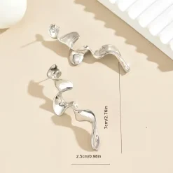 Ένα ζευγάρι μακριά statement σκουλαρίκια σε ασημί-μεταλλική απόχρωση με ρευστό, κυματιστό και αφηρημένο σχήμα, ιδανικά για μια μοντέρνα και εντυπωσιακή εμφάνιση.