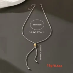 Ασημί κολιέ γραβάτα με χρυσή λεπτομέρεια φορεμένο με κομψό λευκό σακάκι.