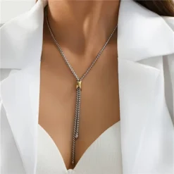 Ασημί κολιέ γραβάτα με χρυσή λεπτομέρεια φορεμένο με κομψό λευκό σακάκι.