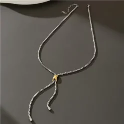 Ασημί κολιέ γραβάτα με χρυσή λεπτομέρεια φορεμένο με κομψό λευκό σακάκι.