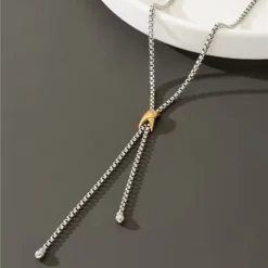 Ασημί κολιέ γραβάτα με χρυσή λεπτομέρεια φορεμένο με κομψό λευκό σακάκι.