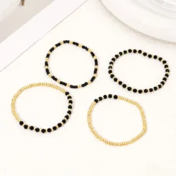 Γυναικείο σετ βραχιόλια με χρυσές χάντρες και μαύρους κρυστάλλους σε λευκό φόντο.