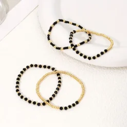 Γυναικείο σετ βραχιόλια με χρυσές χάντρες και μαύρους κρυστάλλους σε λευκό φόντο.