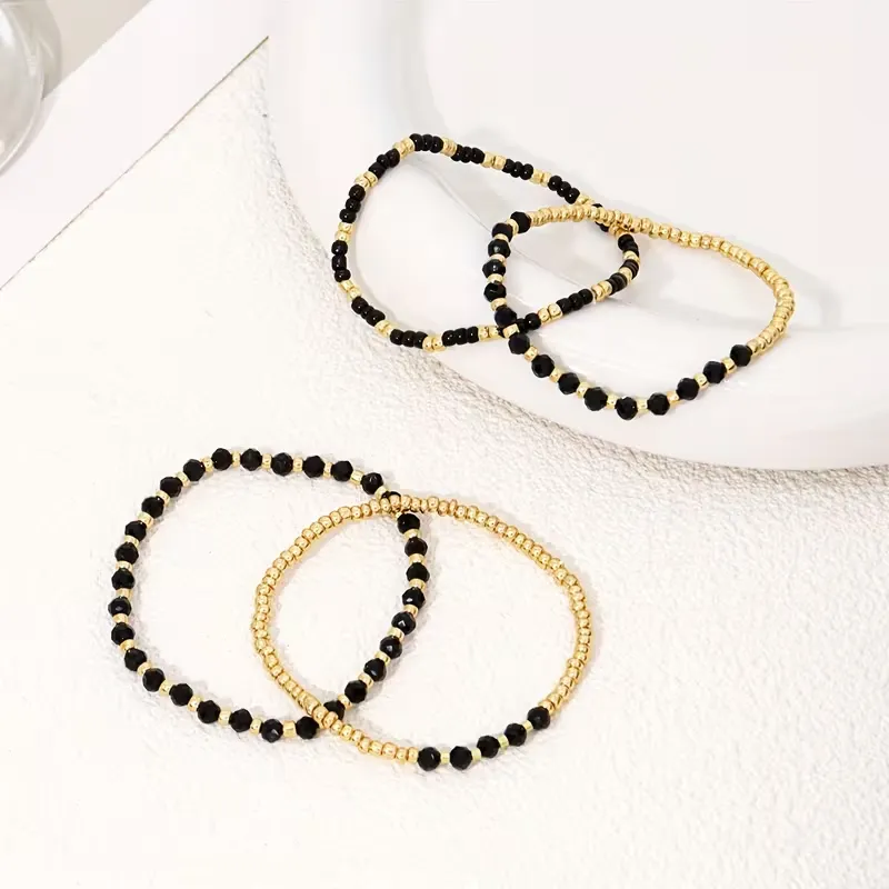 Γυναικείο σετ βραχιόλια με χρυσές χάντρες και μαύρους κρυστάλλους σε λευκό φόντο.