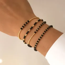 Γυναικείο σετ βραχιόλια με χρυσές χάντρες και μαύρους κρυστάλλους σε λευκό φόντο.