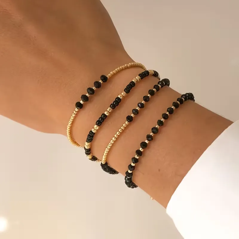 Γυναικείο σετ βραχιόλια με χρυσές χάντρες και μαύρους κρυστάλλους σε λευκό φόντο.