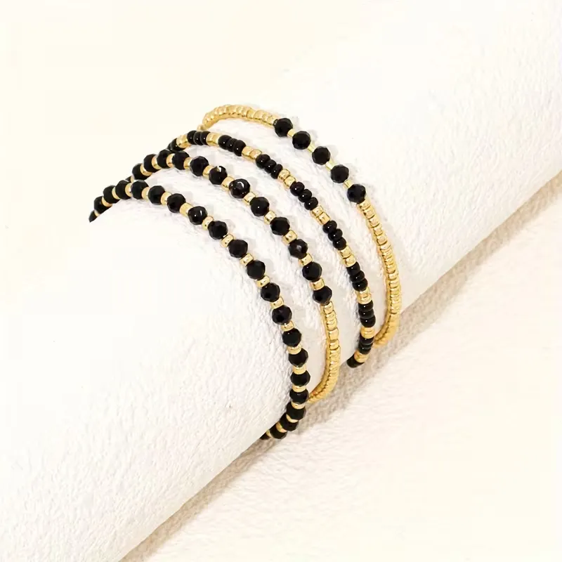 Γυναικείο σετ βραχιόλια με χρυσές χάντρες και μαύρους κρυστάλλους σε λευκό φόντο.