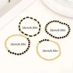 Γυναικείο σετ βραχιόλια με χρυσές χάντρες και μαύρους κρυστάλλους σε λευκό φόντο.