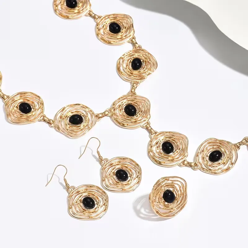 Γυναικείο σετ κοσμημάτων με χρυσό κολιέ, σκουλαρίκια και δαχτυλίδι με μαύρες πέτρες.