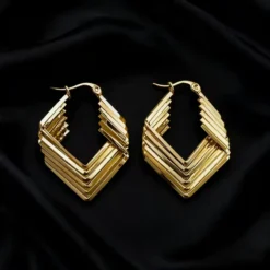 Χρυσά γεωμετρικά σκουλαρίκια κρίκοι με πολυεπίπεδο σχέδιο ρόμβου σε μαύρο φόντο.