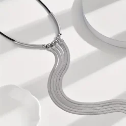 Μακρύ γυναικείο κολιέ με τέσσερις χρυσές αλυσίδες φίδι και μαύρο κορδόνι σε μαύρο φόρεμα.