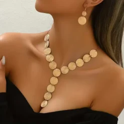 Χρυσό σετ κοσμημάτων με κολιέ και σκουλαρίκια από ανάγλυφους κυκλικούς δίσκους φορεμένο σε μοντέλο.