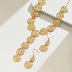 Χρυσό σετ κοσμημάτων με κολιέ και σκουλαρίκια από ανάγλυφους κυκλικούς δίσκους φορεμένο σε μοντέλο.