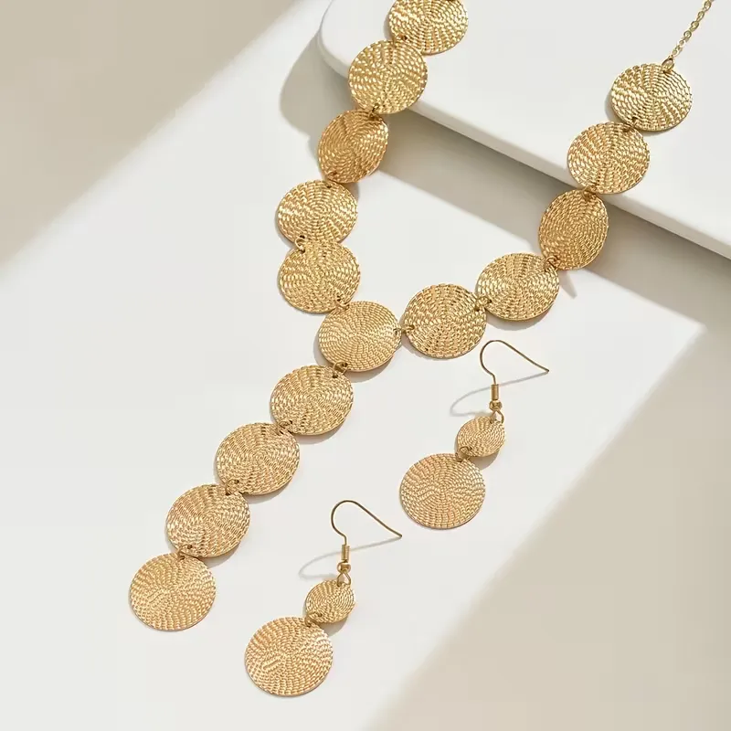 Χρυσό σετ κοσμημάτων με κολιέ και σκουλαρίκια από ανάγλυφους κυκλικούς δίσκους φορεμένο σε μοντέλο.