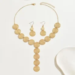 Χρυσό σετ κοσμημάτων με κολιέ και σκουλαρίκια από ανάγλυφους κυκλικούς δίσκους φορεμένο σε μοντέλο.