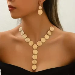 Χρυσό σετ κοσμημάτων με κολιέ και σκουλαρίκια από ανάγλυφους κυκλικούς δίσκους φορεμένο σε μοντέλο.