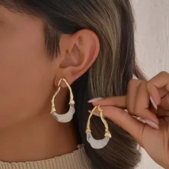 Χρυσά σκουλαρίκια κρίκοι με αφηρημένο σχέδιο και λευκή ρητίνη φορεμένα σε μοντέλο.