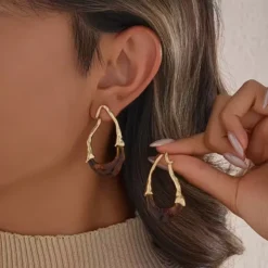 Χρυσά σκουλαρίκια κρίκοι με αφηρημένο σχέδιο και λευκή ρητίνη φορεμένα σε μοντέλο.