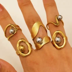 Χρυσά sculptural δαχτυλίδια με ενσωματωμένες ασημί και χρυσές μεταλλικές σφαίρες σε γεωμετρικά σχέδια.