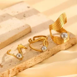 Χρυσά sculptural δαχτυλίδια με ενσωματωμένες ασημί και χρυσές μεταλλικές σφαίρες σε γεωμετρικά σχέδια.