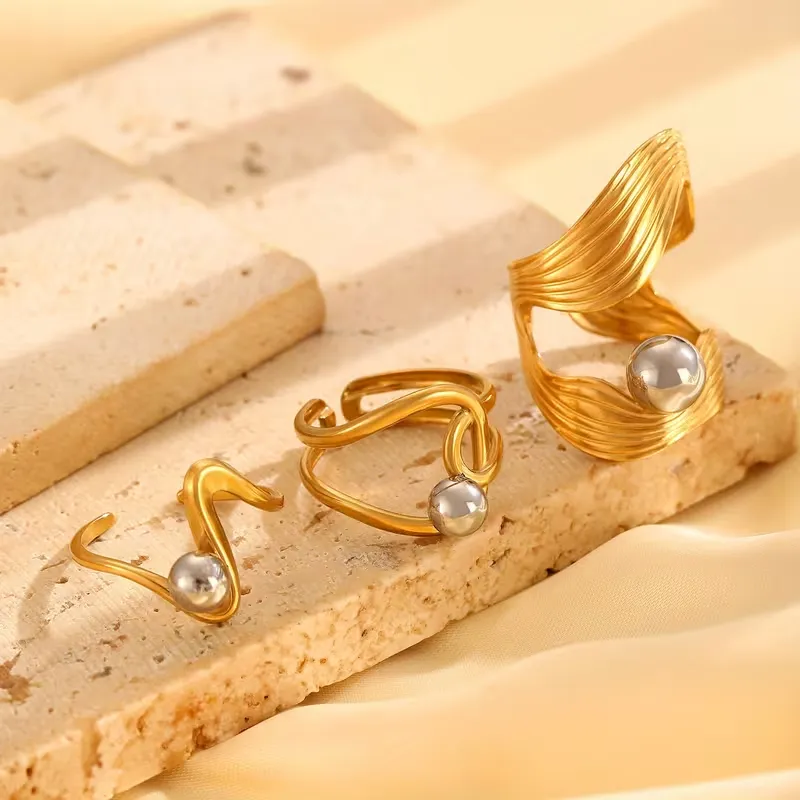 Χρυσά sculptural δαχτυλίδια με ενσωματωμένες ασημί και χρυσές μεταλλικές σφαίρες σε γεωμετρικά σχέδια.