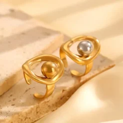 Χρυσά sculptural δαχτυλίδια με ενσωματωμένες ασημί και χρυσές μεταλλικές σφαίρες σε γεωμετρικά σχέδια.