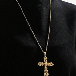 κολιέ με χρυσό σταυρό και λεπτομέρειες από νεκροκεφαλές σε μαύρο φόντο.