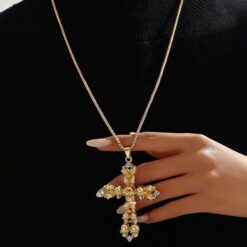 κολιέ με χρυσό σταυρό και λεπτομέρειες από νεκροκεφαλές σε μαύρο φόντο.