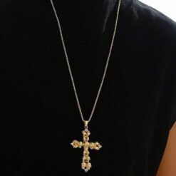 κολιέ με χρυσό σταυρό και λεπτομέρειες από νεκροκεφαλές σε μαύρο φόντο.