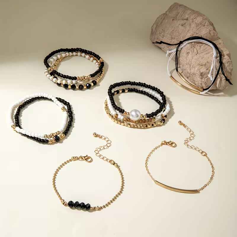 Γυναικείο σετ 12 βραχιόλια με μαύρες λευκές χάντρες πέρλα και χρυσές αλυσίδες σε λευκό φόντο.
