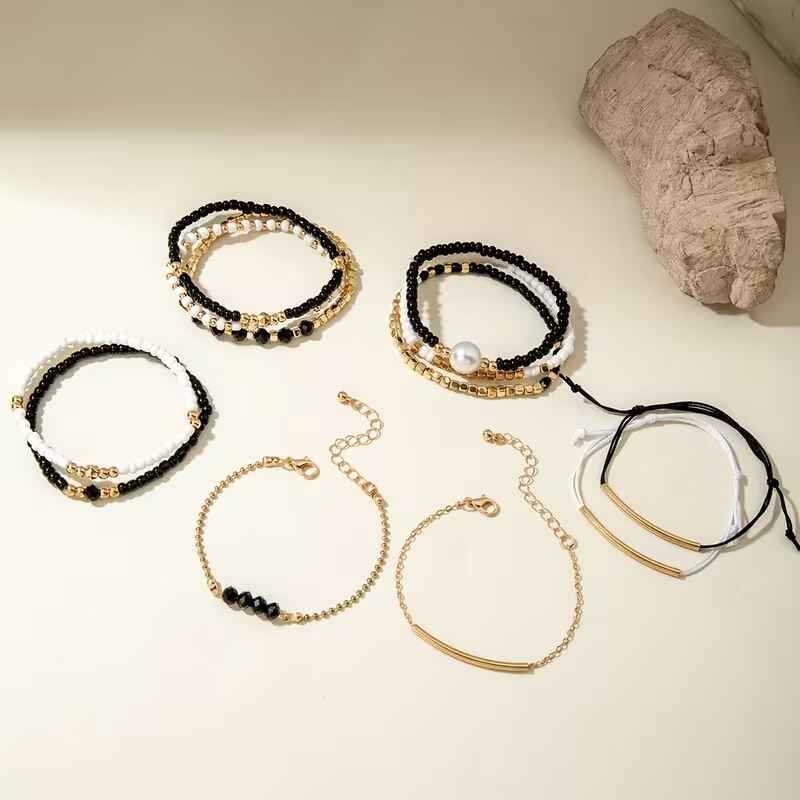 Γυναικείο σετ 12 βραχιόλια με μαύρες λευκές χάντρες πέρλα και χρυσές αλυσίδες σε λευκό φόντο.