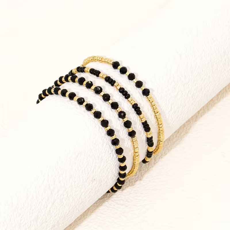Γυναικείο σετ 4 ελαστικά βραχιόλια με μαύρες κρυστάλλινες χάντρες και χρυσές ροδέλες.