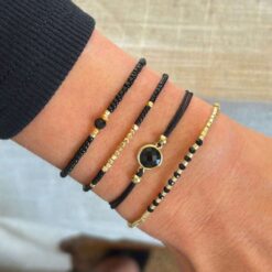 Σετ τεσσάρων γυναικείων βραχιολιών με μαύρες χάντρες και χρυσά στοιχεία φορεμένα σε καρπό.