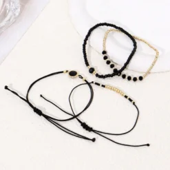 Σετ τεσσάρων γυναικείων βραχιολιών με μαύρες χάντρες και χρυσά στοιχεία φορεμένα σε καρπό.