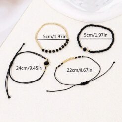 Σετ τεσσάρων γυναικείων βραχιολιών με μαύρες χάντρες και χρυσά στοιχεία φορεμένα σε καρπό.