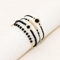 Σετ τεσσάρων γυναικείων βραχιολιών με μαύρες χάντρες και χρυσά στοιχεία φορεμένα σε καρπό.