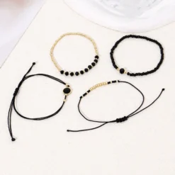 Σετ τεσσάρων γυναικείων βραχιολιών με μαύρες χάντρες και χρυσά στοιχεία φορεμένα σε καρπό.