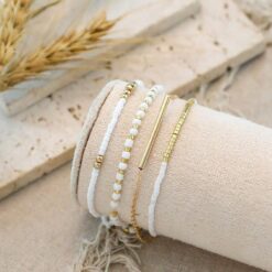 Σετ τεσσάρων γυναικείων βραχιολιών με λευκές χάντρες και χρυσή μεταλλική μπάρα, σε bohemian στυλ.