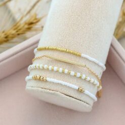 Σετ τεσσάρων γυναικείων βραχιολιών με λευκές χάντρες και χρυσή μεταλλική μπάρα, σε bohemian στυλ.