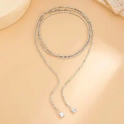 Μακρύ γυναικείο κολιέ σε ασημί χρώμα με μικρά τετράγωνα χαντράκια και μεταλλικές σταγόνες στο τελείωμα,