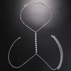 Γυναικείο κόσμημα σώματος body chain σε ασημί χρώμα με σειρά από κρυστάλλινες καρδιές φορεμένο με λευκό σακάκι και μαγιό.