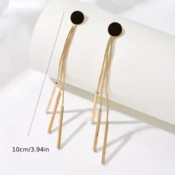 Ζευγάρι μακριά χρυσά γυναικεία σκουλαρίκια με μαύρο κυκλικό στοιχείο και κρεμαστές αλυσίδες σε λευκό φόντο.