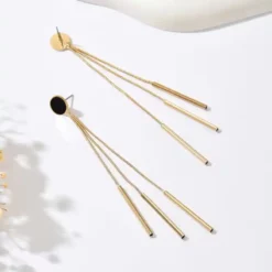 Ζευγάρι μακριά χρυσά γυναικεία σκουλαρίκια με μαύρο κυκλικό στοιχείο και κρεμαστές αλυσίδες σε λευκό φόντο.