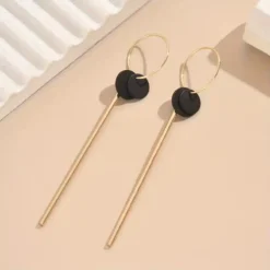 Μακριά γεωμετρικά σκουλαρίκια σε χρυσό χρώμα με μαύρο κυκλικο δίσκο και λεπτή μεταλλική μπάρα, μήκους 9.6 εκατοστών.