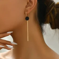 Μακριά γεωμετρικά σκουλαρίκια σε χρυσό χρώμα με μαύρο κυκλικο δίσκο και λεπτή μεταλλική μπάρα, μήκους 9.6 εκατοστών.