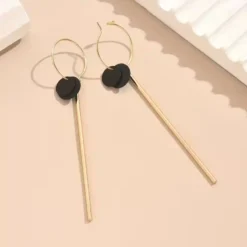 Μακριά γεωμετρικά σκουλαρίκια σε χρυσό χρώμα με μαύρο κυκλικο δίσκο και λεπτή μεταλλική μπάρα, μήκους 9.6 εκατοστών.