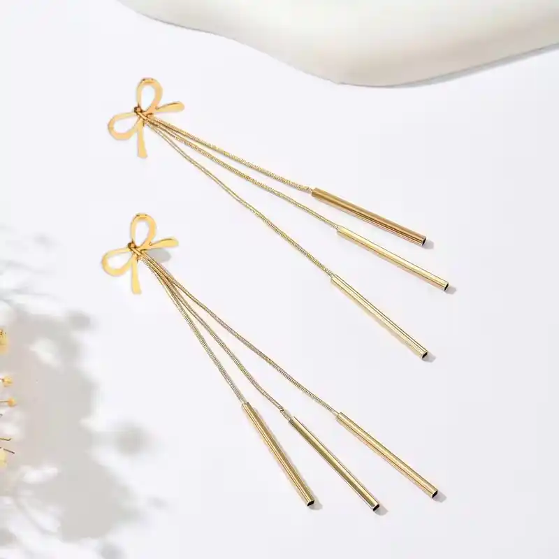 Χρυσά μακριά σκουλαρίκια 10 εκατοστών με σχέδιο φιόγκο και τρεις κρεμαστές λεπτές μπάρες σε λευκό φόντο.