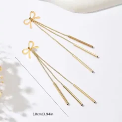 Χρυσά μακριά σκουλαρίκια 10 εκατοστών με σχέδιο φιόγκο και τρεις κρεμαστές λεπτές μπάρες σε λευκό φόντο.