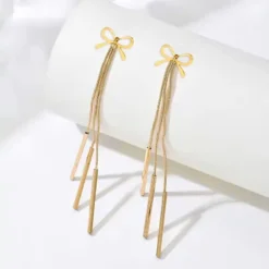 Χρυσά μακριά σκουλαρίκια 10 εκατοστών με σχέδιο φιόγκο και τρεις κρεμαστές λεπτές μπάρες σε λευκό φόντο.